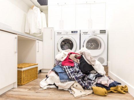 En bunke vasketøj ligger ved en vaskemaskine og tørretumbler